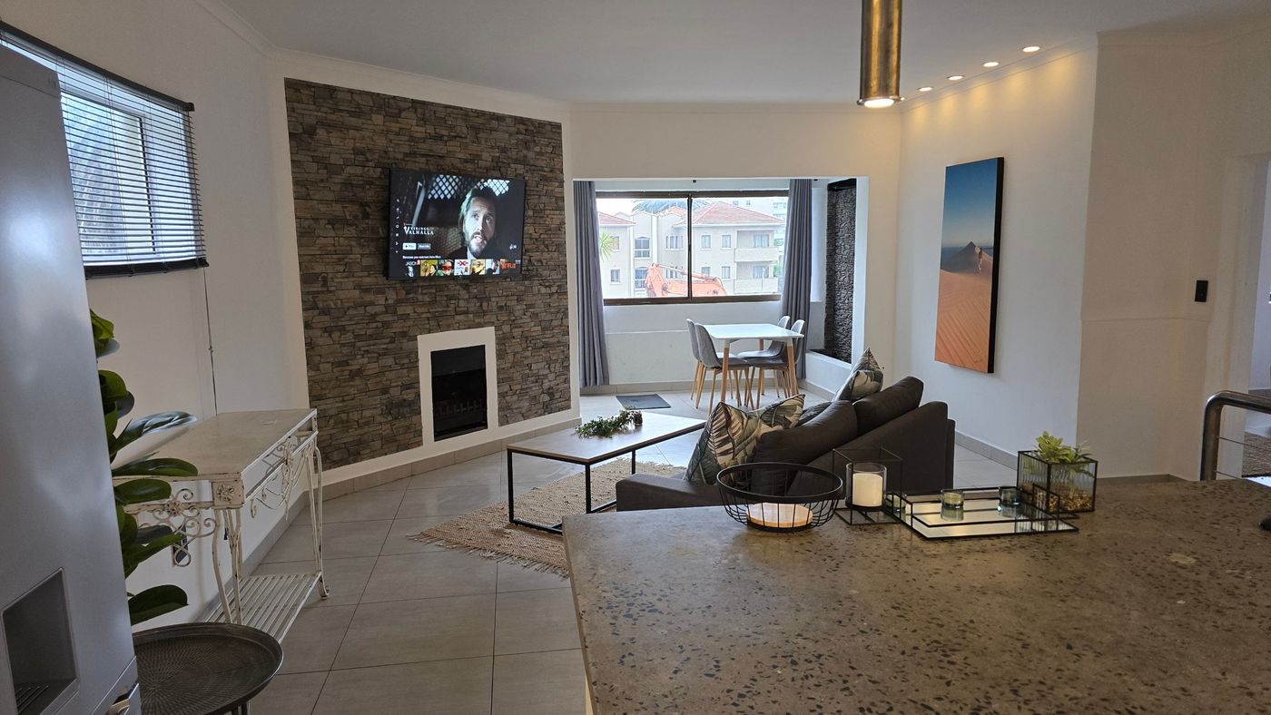 Apartment 10: open-plan lounge with stone feature wall, fireplace, wall-mounted TV and dining table for four